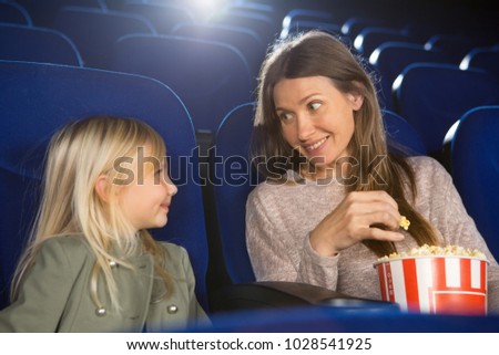 Cheerful mother and daughter smiling at each other enjoying movie premiere at the movie theatre together bonding communication lifestyle people childhood motherhood parenting weekends.