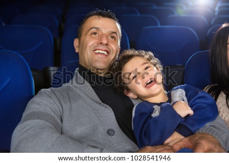 Adorable little boy laughing happily watching a movie with his father at the cinema happiness emotions family positive entertainment bonding fatherhood toddler children kids leisure showtime.