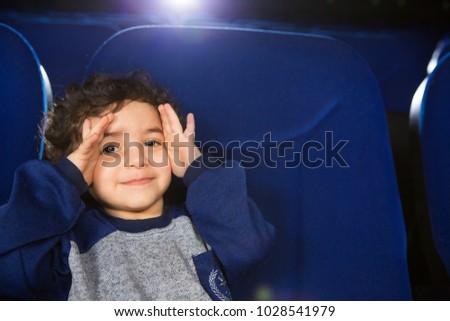 Close up of a little cute Hispanic boy playing peek a boo smiling to the camera sitting at the cinema copyspace family children kids entertaining leisure activity childhood expressive playful.
