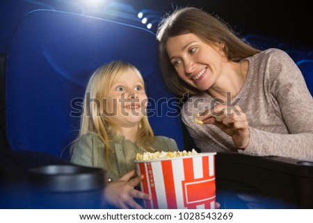 Adorable little girl laughing watchign a cartoon her mom smiling at her with love sitting at the movie theatre copyspace lifestyle leisure motherhood parenting family kids children entertainment