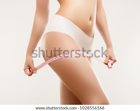 Beautiful slim woman's body. Perfect slim toned young body of the girl. Fitness or plastic surgery and aesthetic cosmetology. Firm buttocks. Beauty girl in white bikini posing on grey background Royalty-Free Stock Photo #1028556166