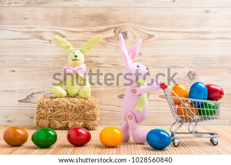 Two easter bunnies with a shopping cart and many colorful easter eggs in front of a wood background