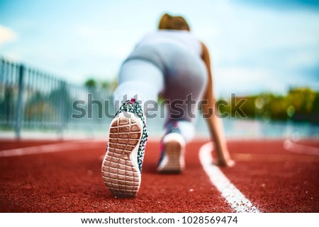 Back view. Young girl legs in stylish sneakers back side on a red race track of a stadium with white lane lines on background. Unrecognizable photo with copy space for inscription or objects