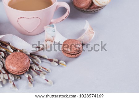 Pink coffee mug with sweet pastel french macaroons and pussy willow on light table from above. Breakfast on Mothers day or Women's day. Tender spring background.