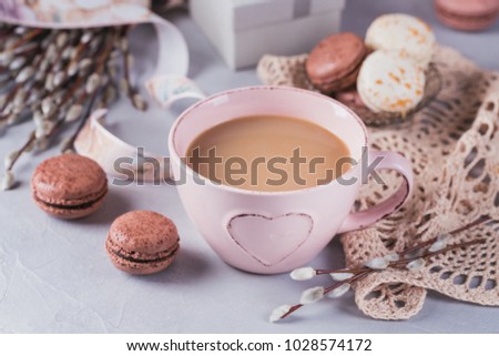 Pink coffee mug with sweet pastel french macaroons, gift box and pussy willow on light table from above. Breakfast on Mothers day or Women's day. Tender spring background.