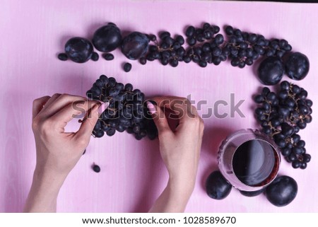 composition of wine, grape and plums on a pink background