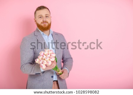 Handsome bearded man holding bouquet of tulips in hand on pink background. 8 march. copy space