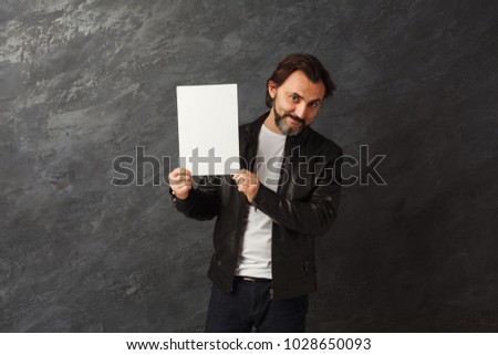 Confident man with blank white board. Successful male in leather jacket holding advertising sheet, copy space