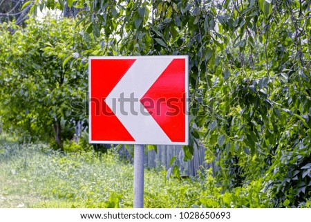 Square road sign indicating the direction of traffic against the background of greenery