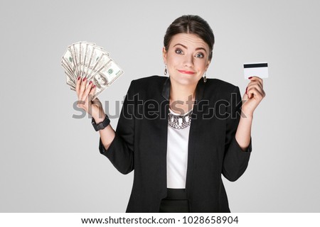 Businesswoman showing at cash, dollar and credit card. Studio shot, indoor. Isolated on grey background