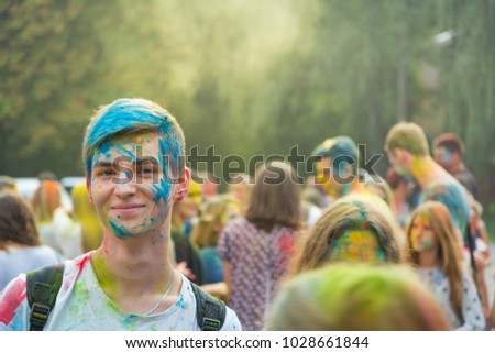Man in color powder looking at camera. Holi celebration. Blurred crowd of people on the background. Portrait photo of smiling student.