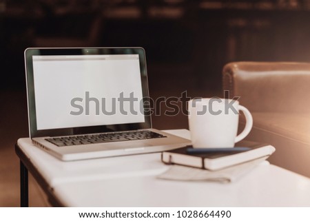 Front view. Empty workplace. On white coffee table is laptop with blank screen, cup of coffee, notebook, pen, newspaper. Place for logo, text, template. Mock up. Telework, distance work online