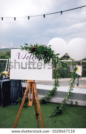 Easel with white frame stands on the roof top during wedding party. Vertical shot
