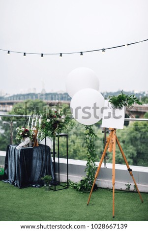 Easel with white frame stands on the roof top during wedding party with trees on background
