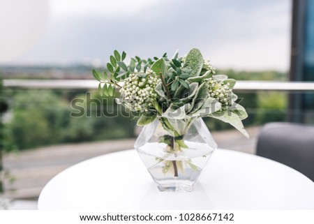 Little glass vase with fresh bouquet stands on the table and trees on background