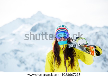 Photo of woman in mask with skis on her shoulder against background of snowy hill