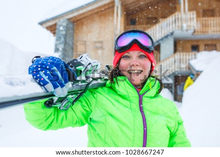 Woman in helmet with skis on shoulder on background of wooden building