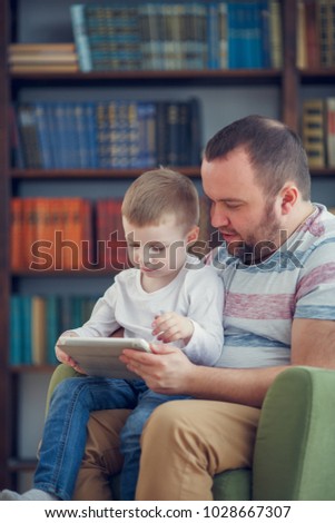 Family image of father and little son sitting with tablet on green chair