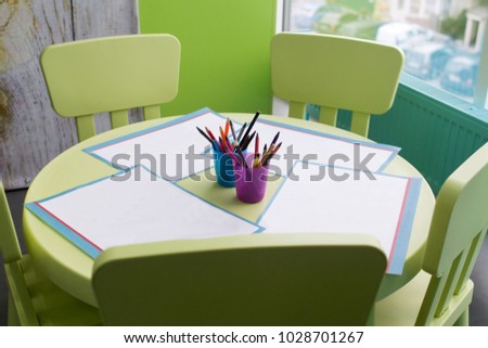 four clean paper blank and colorful pencils on the children's wooden table. and four children's chairs, close-up.