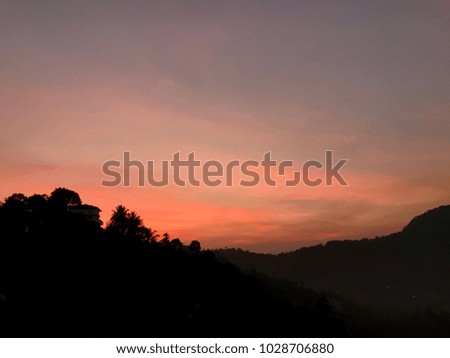 Bright red sunset upon silhouette of house and palm trees in mountains
