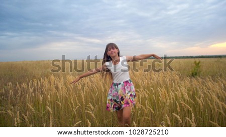 Girl stretching out her arms like wings and walking across field against blue sky smiling. Slow motion.