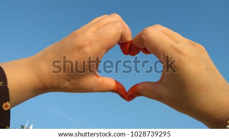 Heart shaped hand over blue sky background

