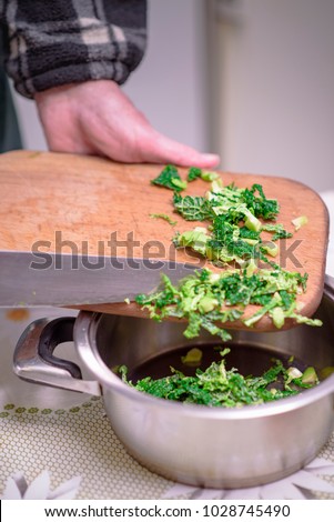 Elderly man, a domestic cook, cutting small pieces of green vegetable, borecole, to prepare for lunch Royalty-Free Stock Photo #1028745490