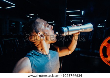 Lifestyle portrait of handsome muscular man drinking water in the gym. Toned image. close up