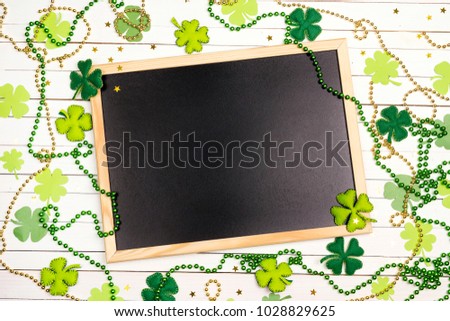 Clean blackboard with felt leaves and beads of clover on white wooden background. Space for text. St.Patrick's day background.
