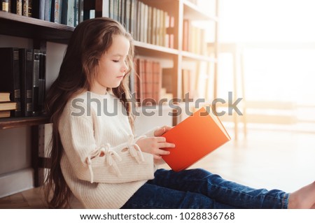 happy smart schoolgirl reading books in library or at home. Kids early learning and education concept.