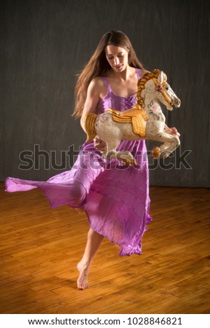 Young woman in flowing lavender dress dancing with an antique carousel horse in the studio.