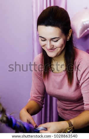 girl in the beauty salon hairdresser is weaved with braids. braided pigtails. Braiding with synthetic purple color kanekalon master staff is smiling.