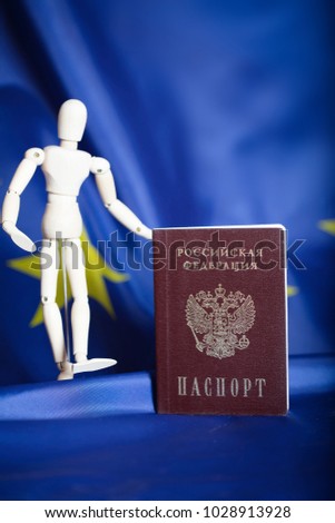 Russian pass and wooden dummy figurine on Russian and European flag. Translation on the pass- Russian Federation. Passport. Closeup