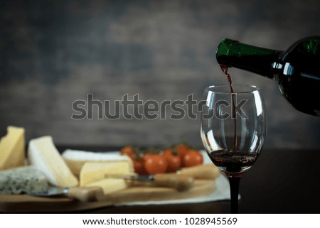 Pouring red wine above board of cheese