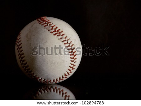Well used baseball on a black reflective surface