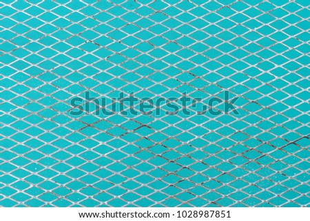 close up silver gray steel mesh in front of blue concrete wall background, diagonal repetitive pattern of old metallic grating for hanging merchandise to display in stall at flea market