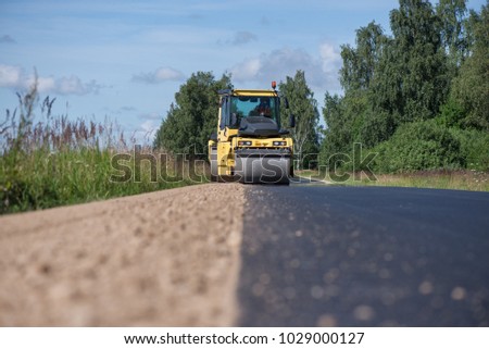 Yellow heavy vibration roller at asphalt pavement works. Road repairing in city. Road construction workers repairing highway road on sunny summer day. Heavy machinery, loaders and trucks.
