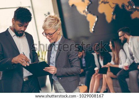 Businessman and businesswoman reviewing contract; business team working in the background Royalty-Free Stock Photo #1029008167