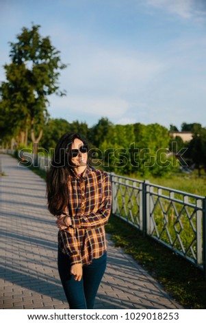 Girl in sunglasses and a plaid shirt walks through the city, smiling