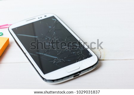 Scratched and broken smartphone on white wooden table background. Anger concept.