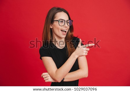 Image of cheerful woman with long brown hair winking and showing index finger aside meaning hey you isolated over red background