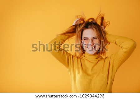 Trendy beautiful hipster girl.Smiling young girl in stylish glasses with yellow background wearing fashion clothes