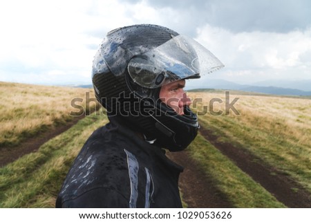 Close up portrait of confident motorbiker wearing helmet and jacket staring at camera with eyes full of determination, ready for motor race on summer day outdoors. off road travel touring concept