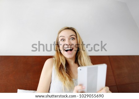 beautiful pretty woman happy shocked face with tablet looking at camera at white bed. surprised girl amazed in shock and surprise happiness and excited