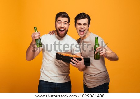 Portrait of a two excited young men watching football while drinking beer and eating pizza isolated over yellow background