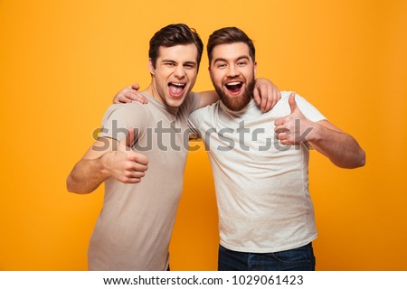 Portrait of a two happy young men showing thumbs up isolated over yellow background Royalty-Free Stock Photo #1029061423