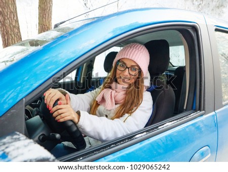 girl in a pink hat driving a blue car in winter