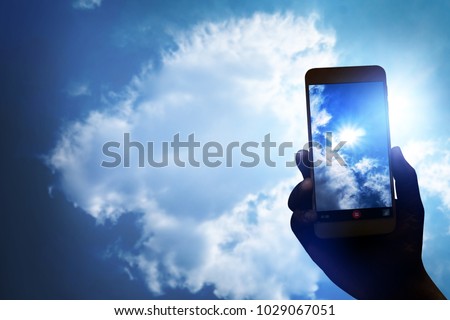 Hand holding smartphone for recording video and take photo the sun clouds sky, hi technology photography.