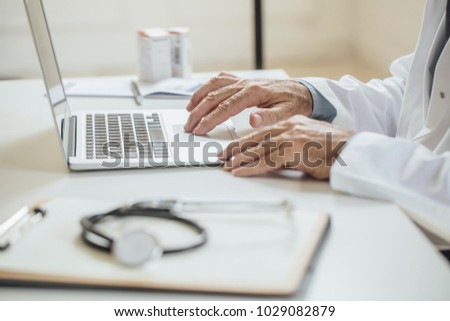 Hands of unrecognisable man doctor sitting at his office and typing on his laptop.