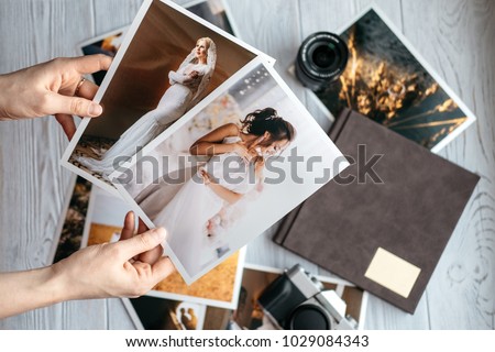Printed wedding photos with the bride and groom, a vintage black camera, photoalbum and woman hands with two photos Royalty-Free Stock Photo #1029084343